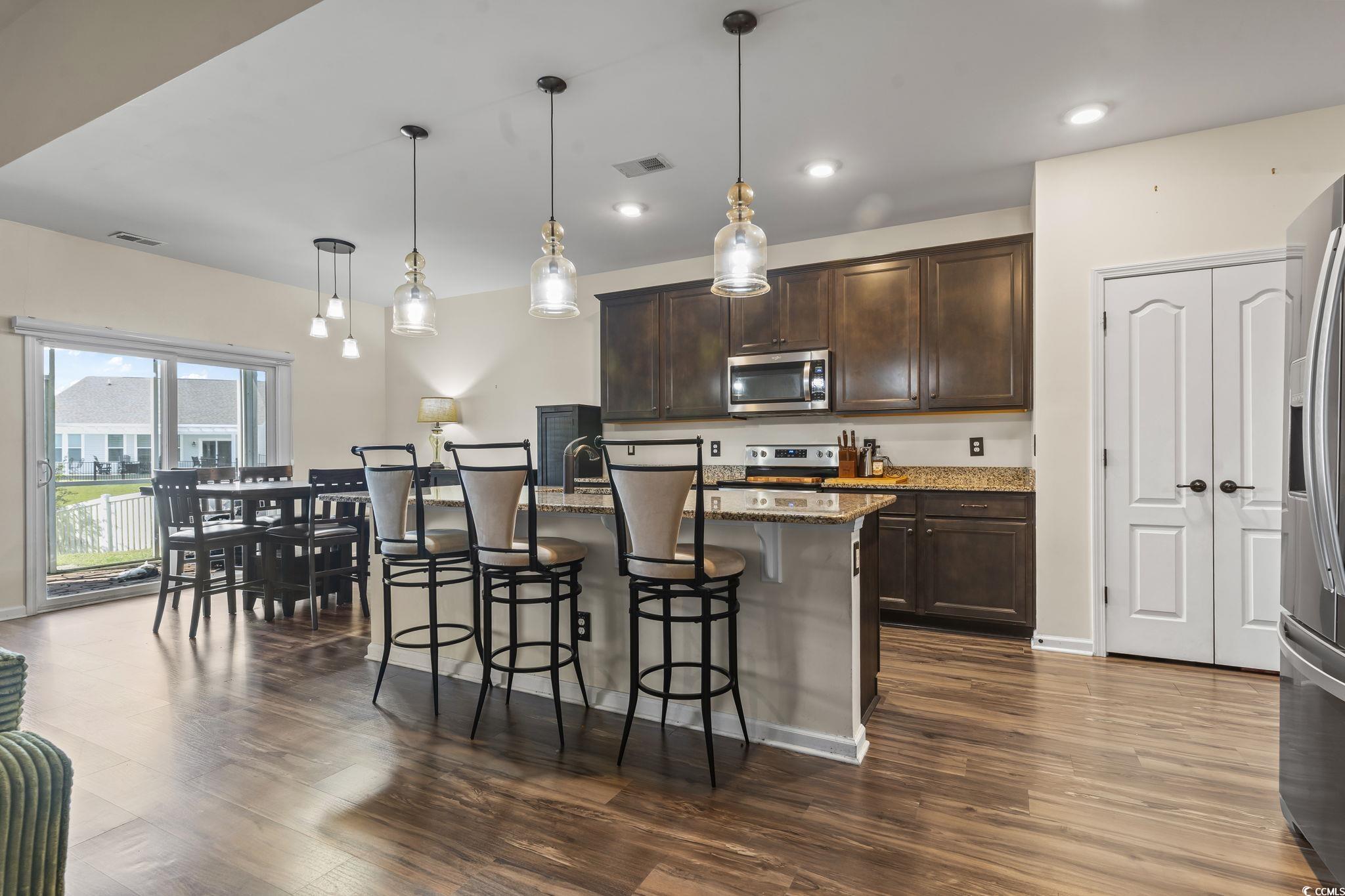 256 Copper Leaf Drive Myrtle Beach, SC 29588 - Photo 8 of 40 Kitchen with dark brown cabinets, light stone counters, a kitchen breakfast bar, decorative light fixtures, and recessed lighting