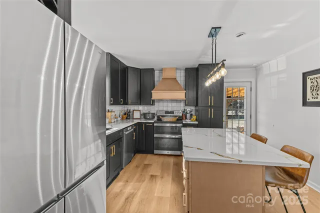 a kitchen with stainless steel appliances granite countertop a refrigerator a sink dishwasher a stove and white countertops with wooden floor