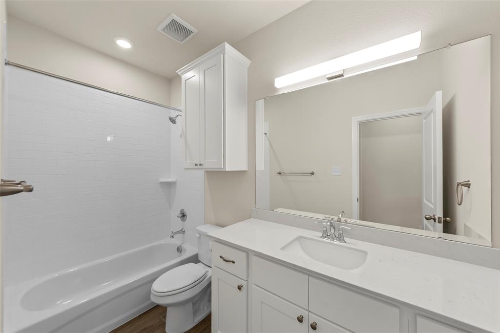 1508 Addison Lane Lancaster, TX 75134 - Photo 14 of 20 Bathroom featuring a white subway tile shower surround, a built-in white cabinet, a full-width mirror, a vanity with a white countertop and integrated sink, and wood-finish flooring