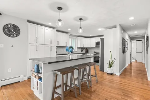 a kitchen with stainless steel appliances granite countertop a refrigerator a sink dishwasher a stove and white cabinets with wooden floor