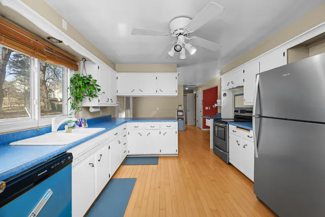 a kitchen with stainless steel appliances a stove a sink dishwasher a refrigerator white cabinets and wooden floor