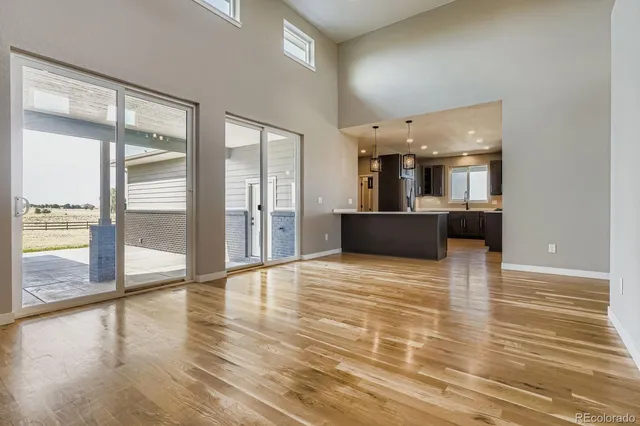 a view of an empty room with wooden floor and a kitchen