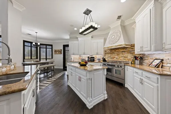 a kitchen with granite countertop a stove a sink dishwasher a dining table and chairs with wooden floor