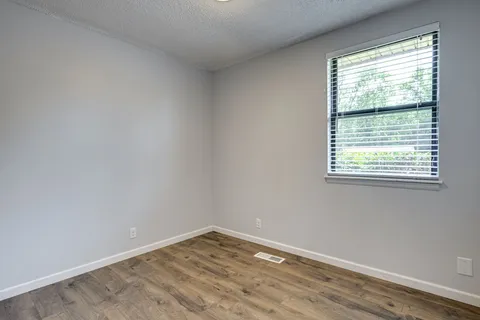 a view of an empty room with wooden floor and a window