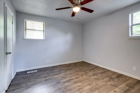 an empty room with wooden floor fan and windows
