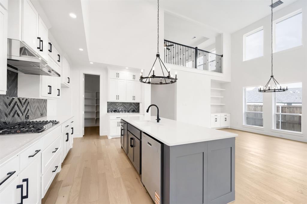 733 Red Cedar Road Haslet, TX 76052 - Photo 8 of 28 Modern kitchen featuring white cabinetry, black hardware, stainless steel appliances, a gray island with a white countertop, and herringbone tile backsplashes