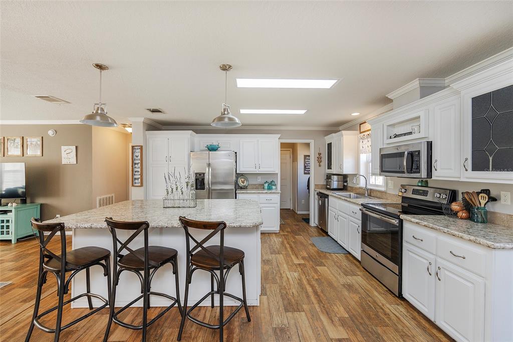 2100 East Kicklighter Road Lake Helen, FL 32744 - Photo 13 of 61 a kitchen with stainless steel appliances kitchen island granite countertop a stove top oven a sink dishwasher a dining table and chairs with wooden floor