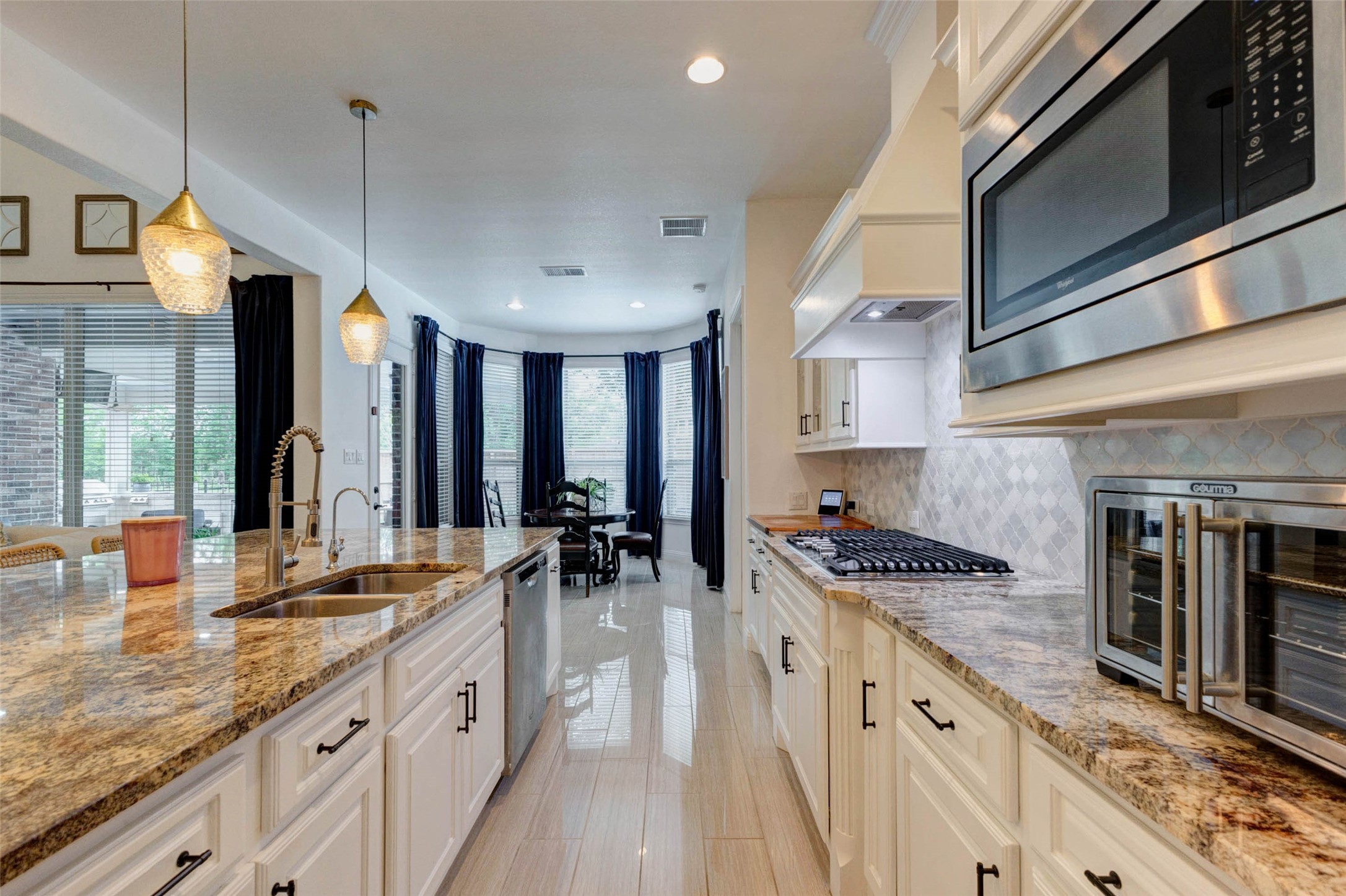 29903 Spring Side Court Fulshear, TX 77406 - Photo 14 of 50 The kitchen is equipped with a gas cooktop, built in microwave, and a beautifully designed vent hood that perfectly complements the painted white cabinetry. A stylish backsplash adds texture and visual appeal to the space.