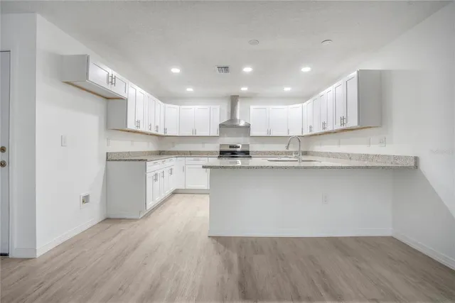 a kitchen with kitchen island granite countertop wooden floors white cabinets and stainless steel appliances