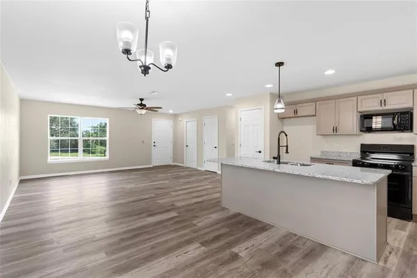 a large kitchen with granite countertop a stove a sink a center island and wooden floor