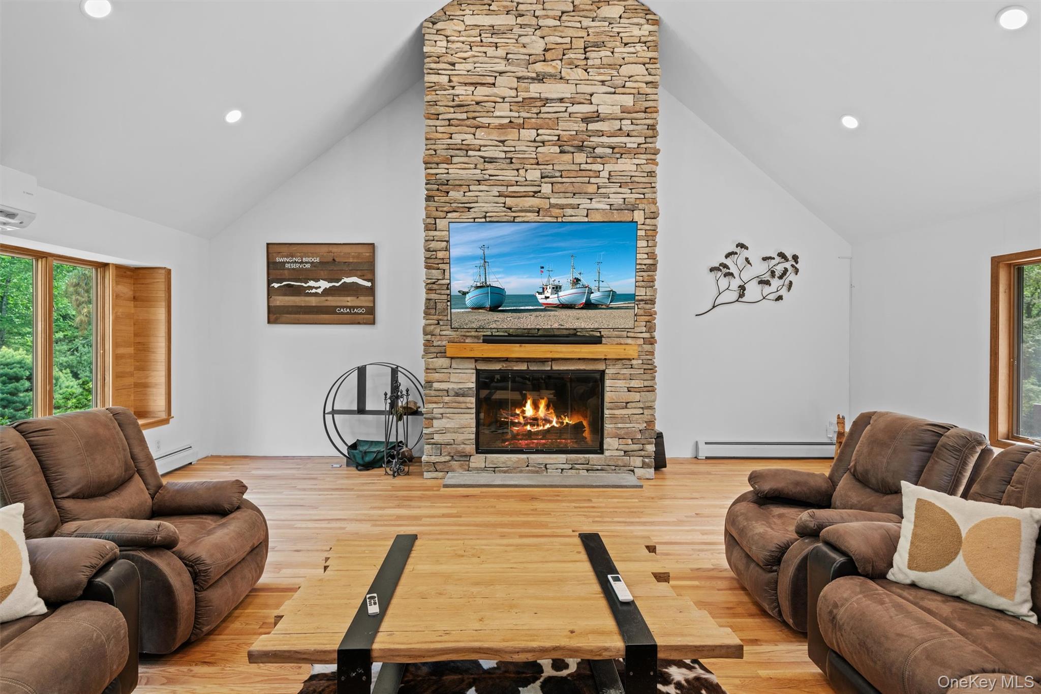 1775 Plank Rd Section A Forestburgh, NY 12777 - Photo 7 of 50 Living room with high vaulted ceiling, a baseboard heating unit, a stone fireplace, healthy amount of natural light, and wood finished floors