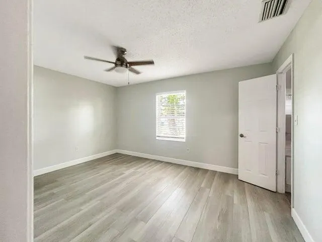 an empty room with wooden floor ceiling fan and windows
