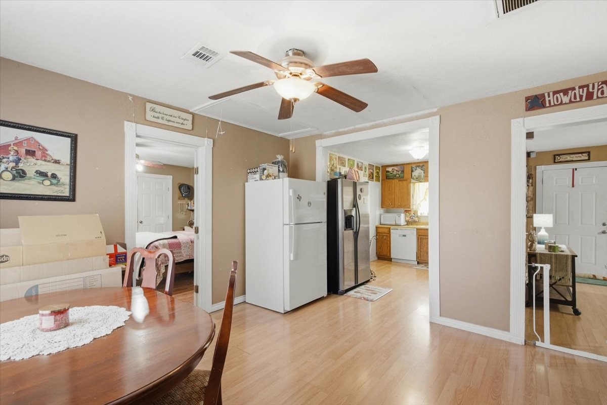 765 Norcross Road Wallis, TX 77485 - Photo 9 of 42 This cozy home features a central dining area with warm vinyl wood flooring and a ceiling fan. It's connected to a spacious kitchen with ample cabinetry and modern appliances. The layout provides easy access to adjacent rooms, ideal for seamless living and entertaining.
