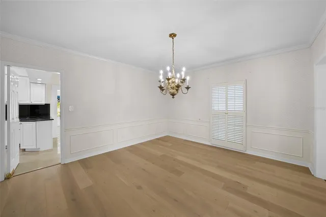 a view of an empty room with chandelier and kitchen