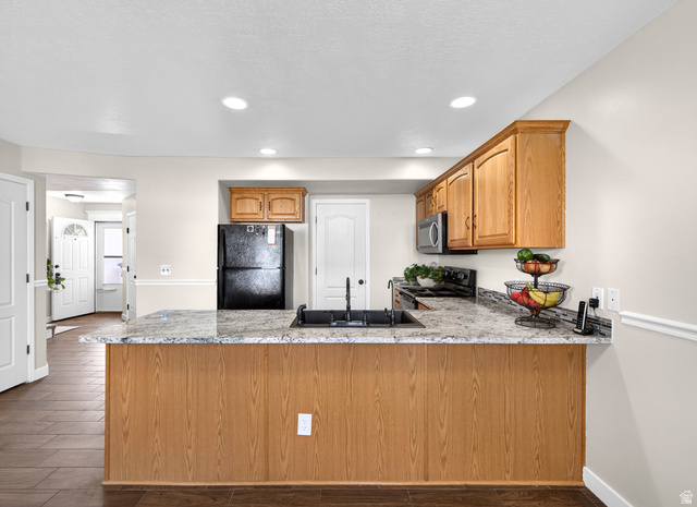 Kitchen with a peninsula, dark wood-type flooring, black appliances, wood finish cabinetry, and recessed lighting