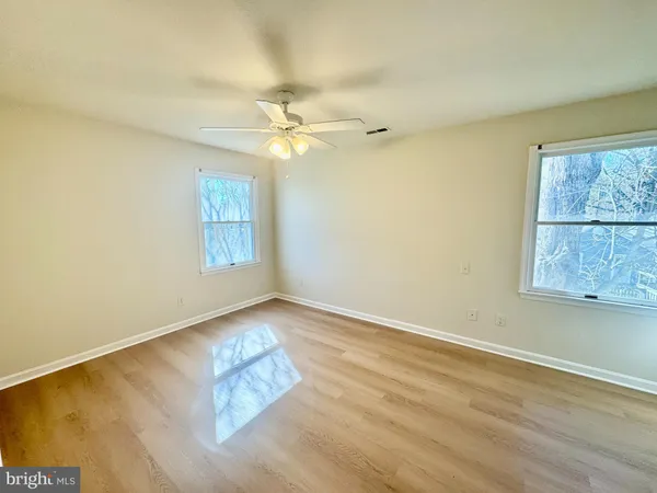 an empty room with wooden floor fan and windows