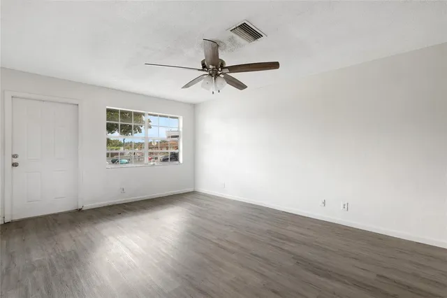 an empty room with wooden floor ceiling fan and windows