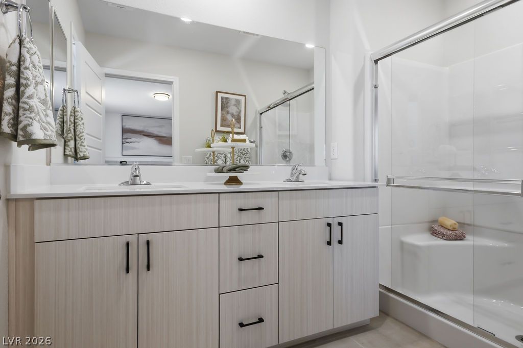 913 Cadence View Way Henderson, NV 89011 - Photo 30 of 46 A well-lit primary bathroom features a double vanity and a glass-enclosed shower with clean lines.