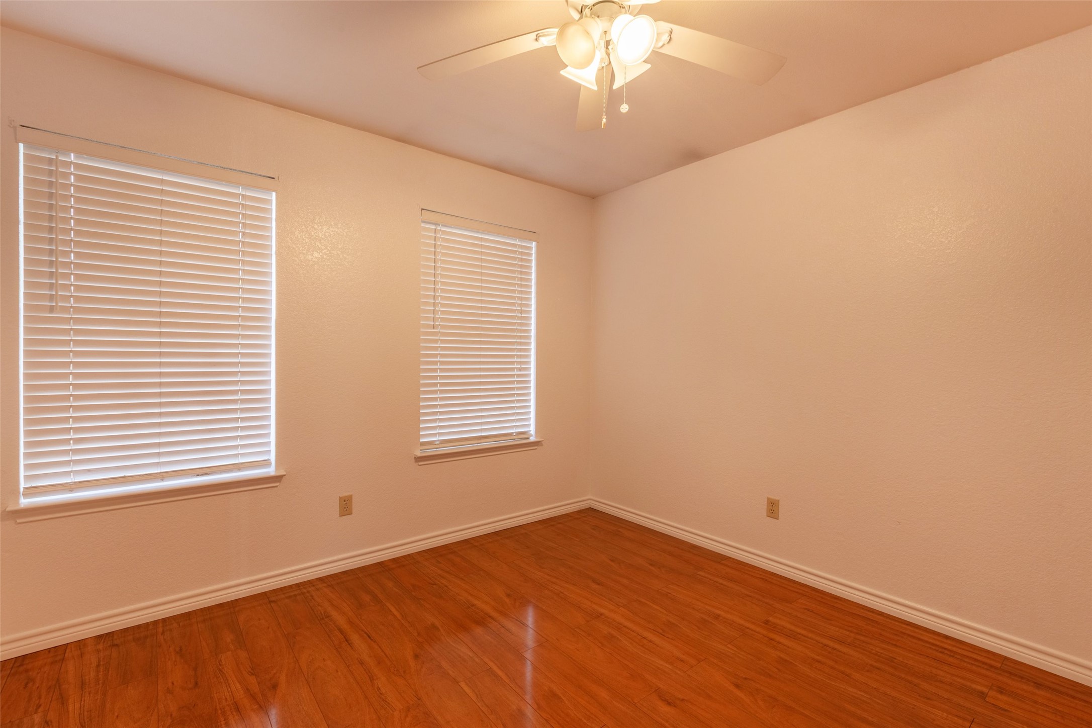 8506 Bisbee Court Austin, TX 78745 - Photo 10 of 20 Room featuring wood-finish flooring, two windows with blinds, white baseboards, and a ceiling fan with integrated lighting