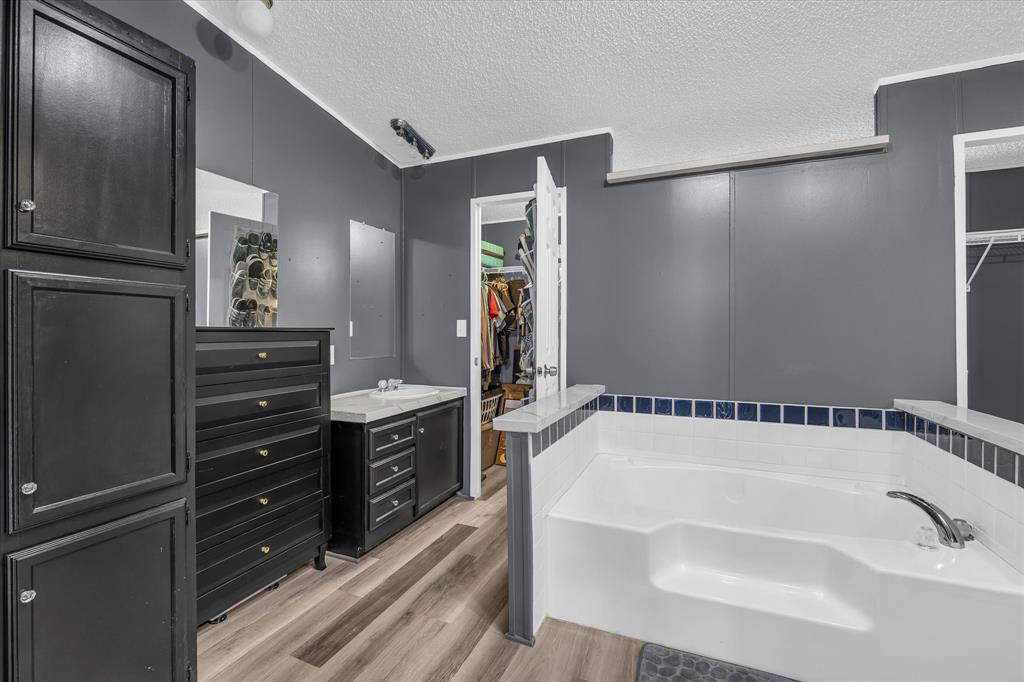 3615 Spring Valley Road Lorena, TX 76655 - Photo 21 of 33 Integrated soaking tub with tiled surround, wood-finish flooring, and a vanity with a countertop and sink