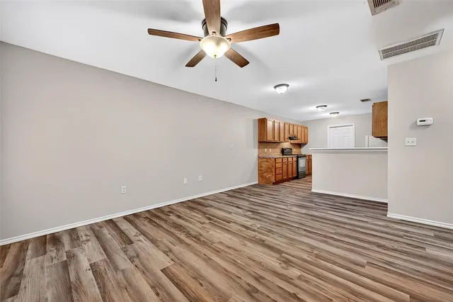 a view of empty room with wooden floor and kitchen view