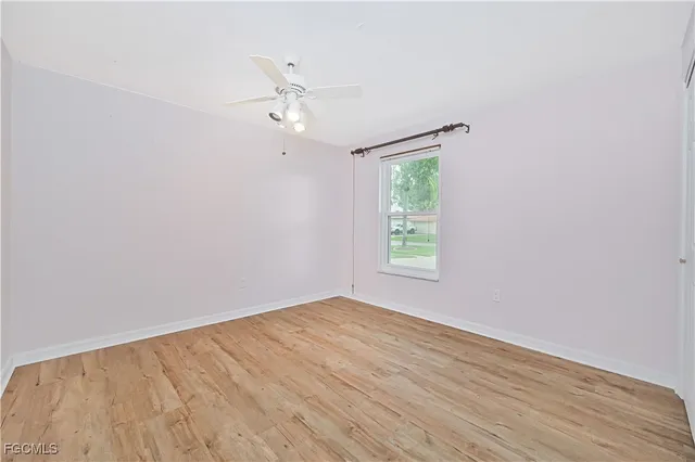 an empty room with wooden floor chandelier fan and windows