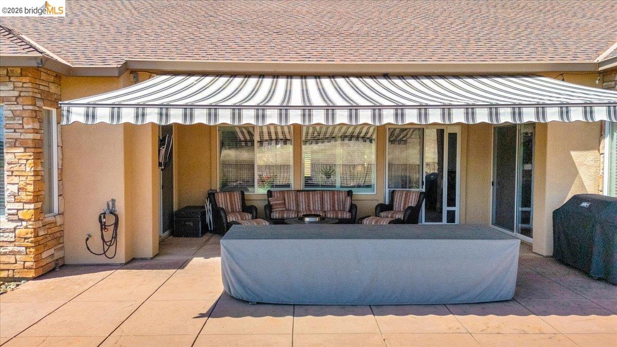 158 Rock Ridge Lane Copperopolis, CA 95228 - Photo 52 of 72 Expansive outdoor patio featuring a large retractable awning, stone siding accents, a durable shingle roof, and multiple large windows