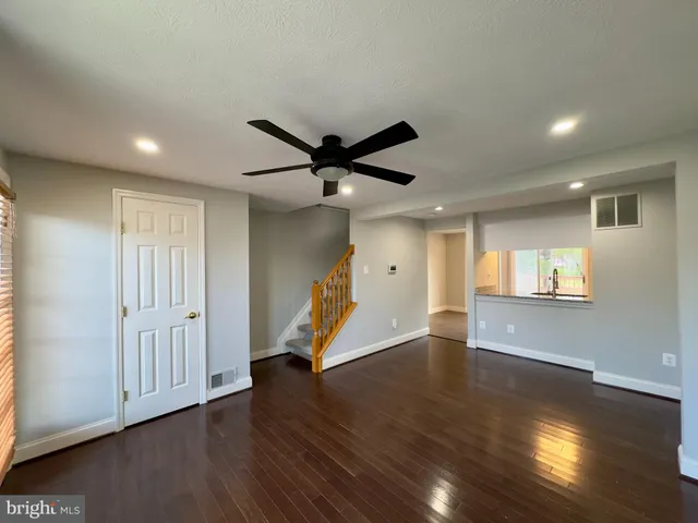 a view of an empty room with wooden floor and a ceiling fan