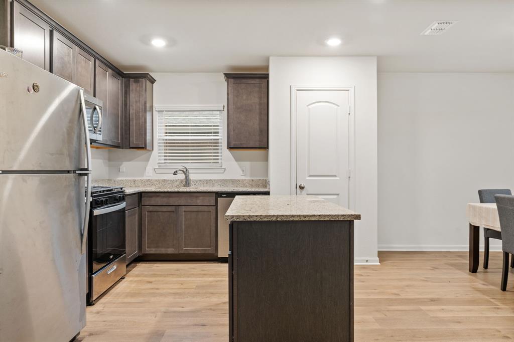 8216 Columbia Falls Road Ponder, TX 76259 - Photo 4 of 28 Kitchen with light stone countertops, dark brown cabinets, light wood-type flooring, a sink, and stainless steel appliances