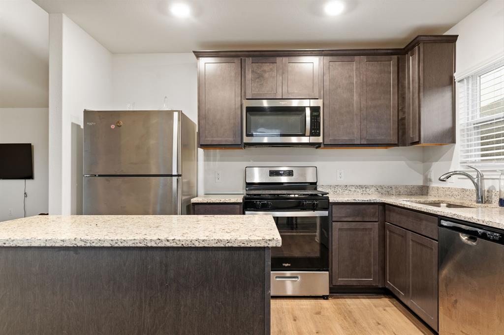8216 Columbia Falls Road Ponder, TX 76259 - Photo 5 of 28 Kitchen with dark brown cabinetry, light stone countertops, a sink, light wood finished floors, and stainless steel appliances