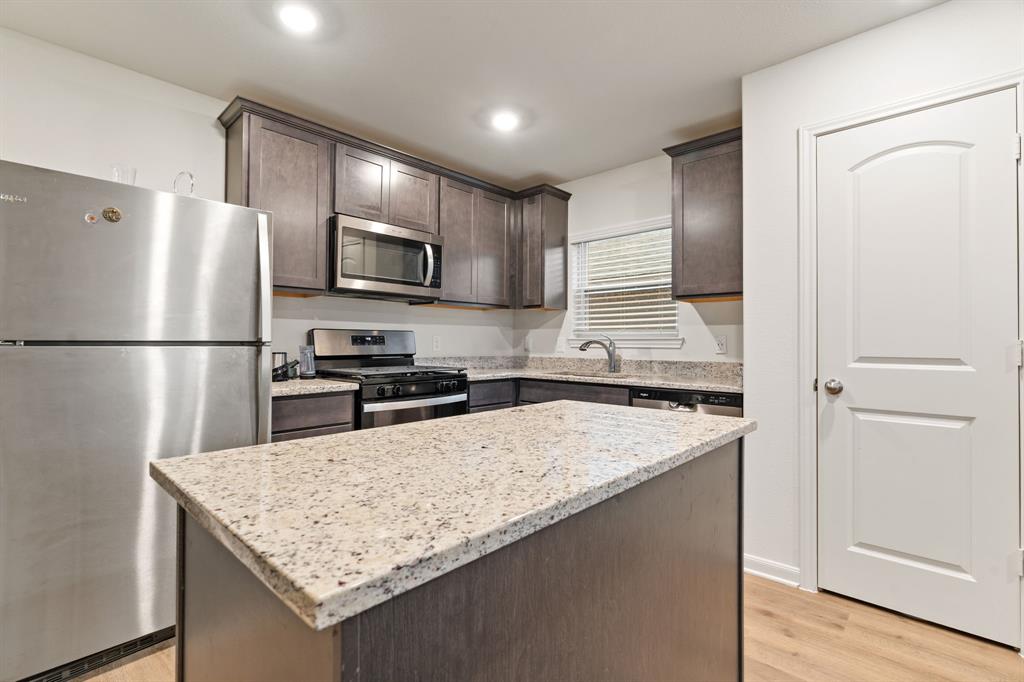 8216 Columbia Falls Road Ponder, TX 76259 - Photo 6 of 28 Kitchen featuring dark brown cabinets, light stone counters, light wood-style floors, stainless steel appliances, and a kitchen island