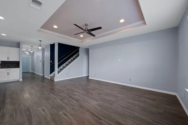 a view of an empty room with wooden floor a ceiling fan and kitchen space