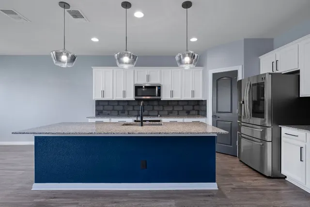 a large kitchen with granite countertop a stove a sink a center island a refrigerator and a wooden floor