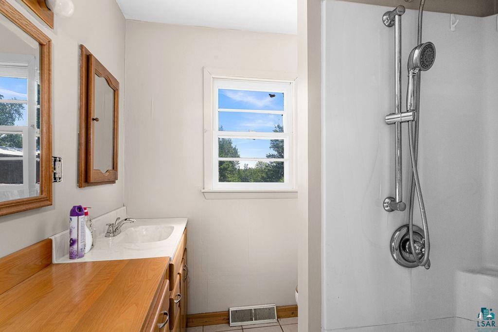 2592 Strandberg Road Barnum, MN 55707 - Photo 13 of 44 Bathroom featuring a white shower stall with an adjustable showerhead, a single window, a vanity with a white countertop and integrated sink, and an additional wood-finish countertop space