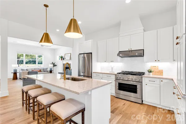 a kitchen with stainless steel appliances granite countertop a stove a sink a refrigerator a dining table and chairs with wooden floor