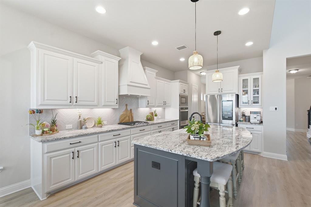 313 Tate Lane Anna, TX 75409 - Photo 12 of 30 Modern kitchen featuring white cabinetry, a large kitchen island with a stone countertop, stainless steel appliances, and wood-finish flooring