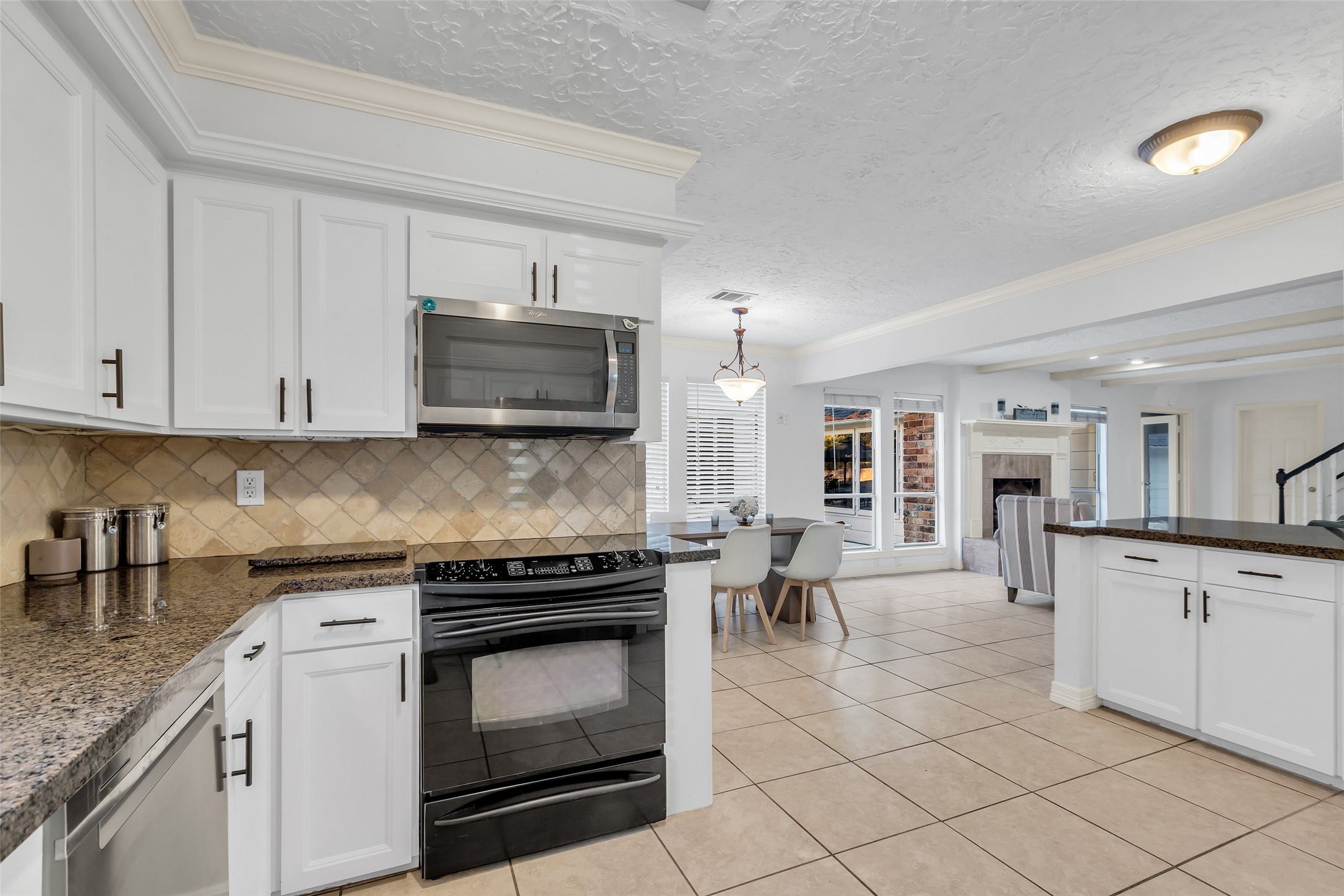 24102 Northcrest Drive Spring, TX 77389 - Photo 8 of 31 This home features a spacious open kitchen and dining area with modern appliances, white cabinetry, and a cozy living space with a fireplace. The tile flooring and large windows create a bright, inviting atmosphere.