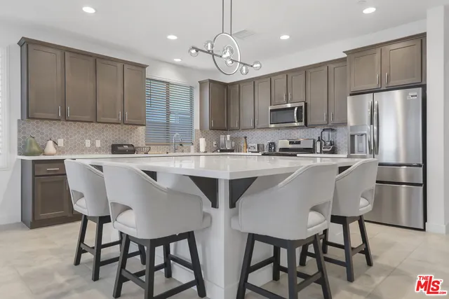 a kitchen with stainless steel appliances granite countertop a dining table chairs refrigerator and microwave