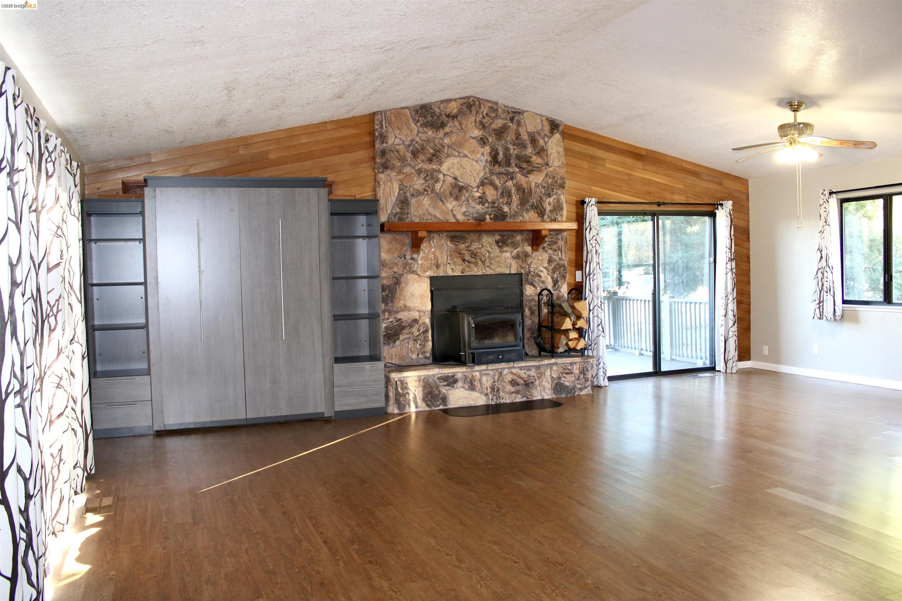 13033 Clements Road Groveland, CA 95321 - Photo 10 of 23 living room featuring wood walls, a ceiling fan, dark wood flooring, and a wood stove