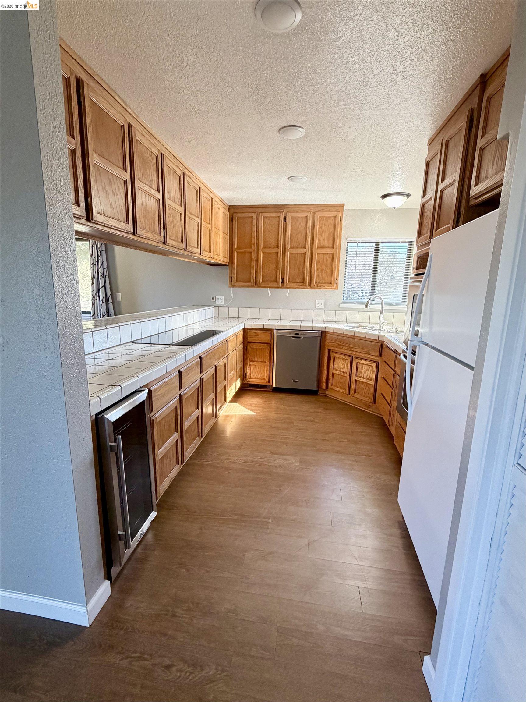 13033 Clements Road Groveland, CA 95321 - Photo 11 of 23 Kitchen with tile counters, wood finish cabinets, dark wood-style flooring, freestanding refrigerator, and wine cooler