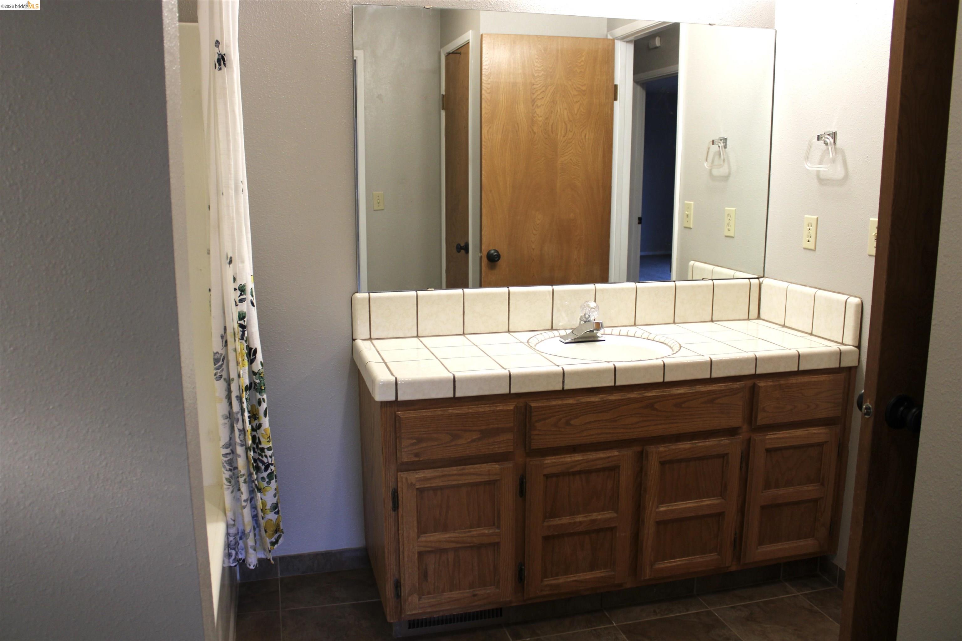 13033 Clements Road Groveland, CA 95321 - Photo 19 of 23 Bathroom connected to bedroom with vanity, a textured wall, dark tile patterned flooring, and shower / tub combo