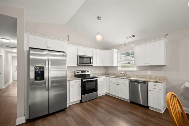 a kitchen with stainless steel appliances granite countertop a stove a sink dishwasher a refrigerator and white cabinets with wooden floor