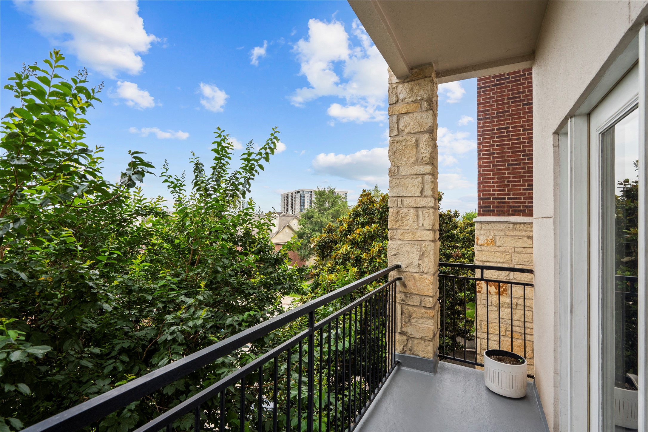 1900 Genesee Street, Unit 203 Houston, TX 77006 - Photo 23 of 30 This photo showcases a cozy balcony featuring a sturdy metal railing and stone columns. It offers lush green views, creating a serene outdoor space, perfect for relaxation. The balcony is adjacent to glass doors, allowing easy indoor-outdoor access.
