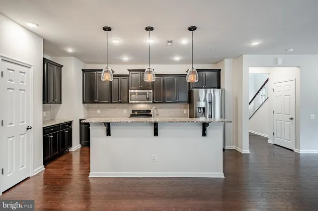 a kitchen with stainless steel appliances kitchen island granite countertop a refrigerator a stove a oven and a wooden floors