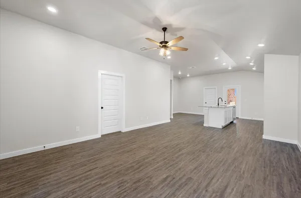 a view of an empty room with wooden floor and a ceiling fan