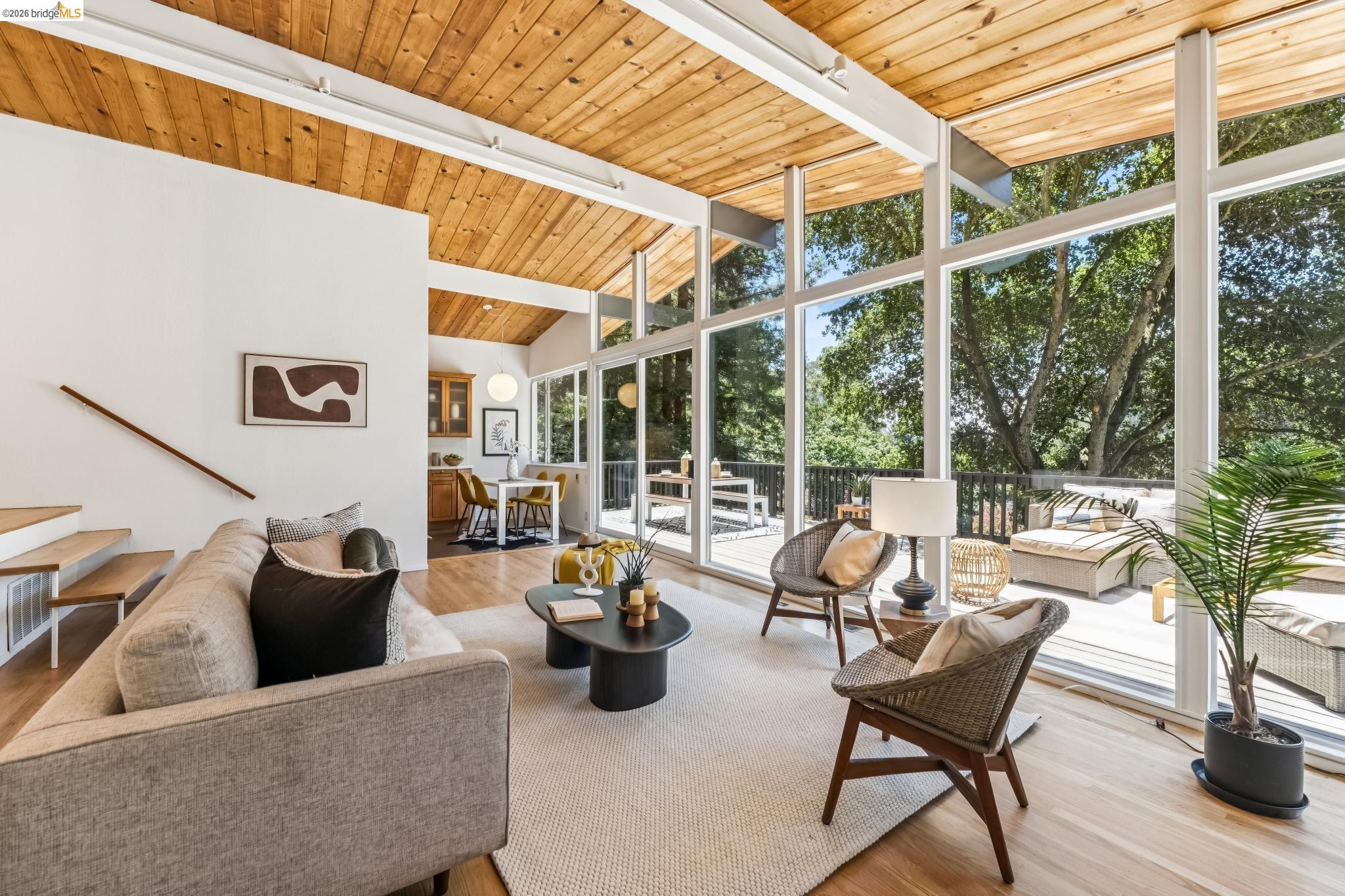 6645 Heather Ridge Way Oakland, CA 94611 - Photo 17 of 61 Vaulted wood-paneled ceiling with exposed beams, full-height window walls, wood-finish flooring, and an expansive exterior deck with surrounding trees