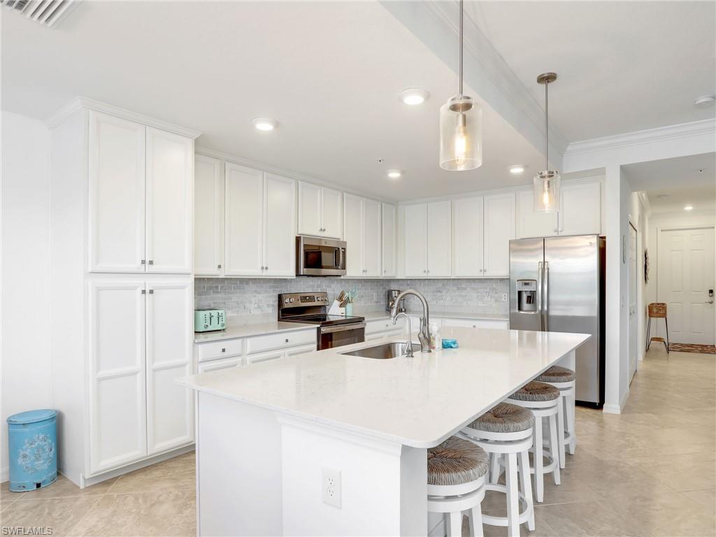 a kitchen with stainless steel appliances a microwave a stove a sink a refrigerator and white cabinets with wooden floor