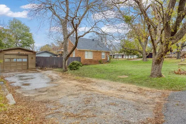 a backyard of a house with plants and large tree