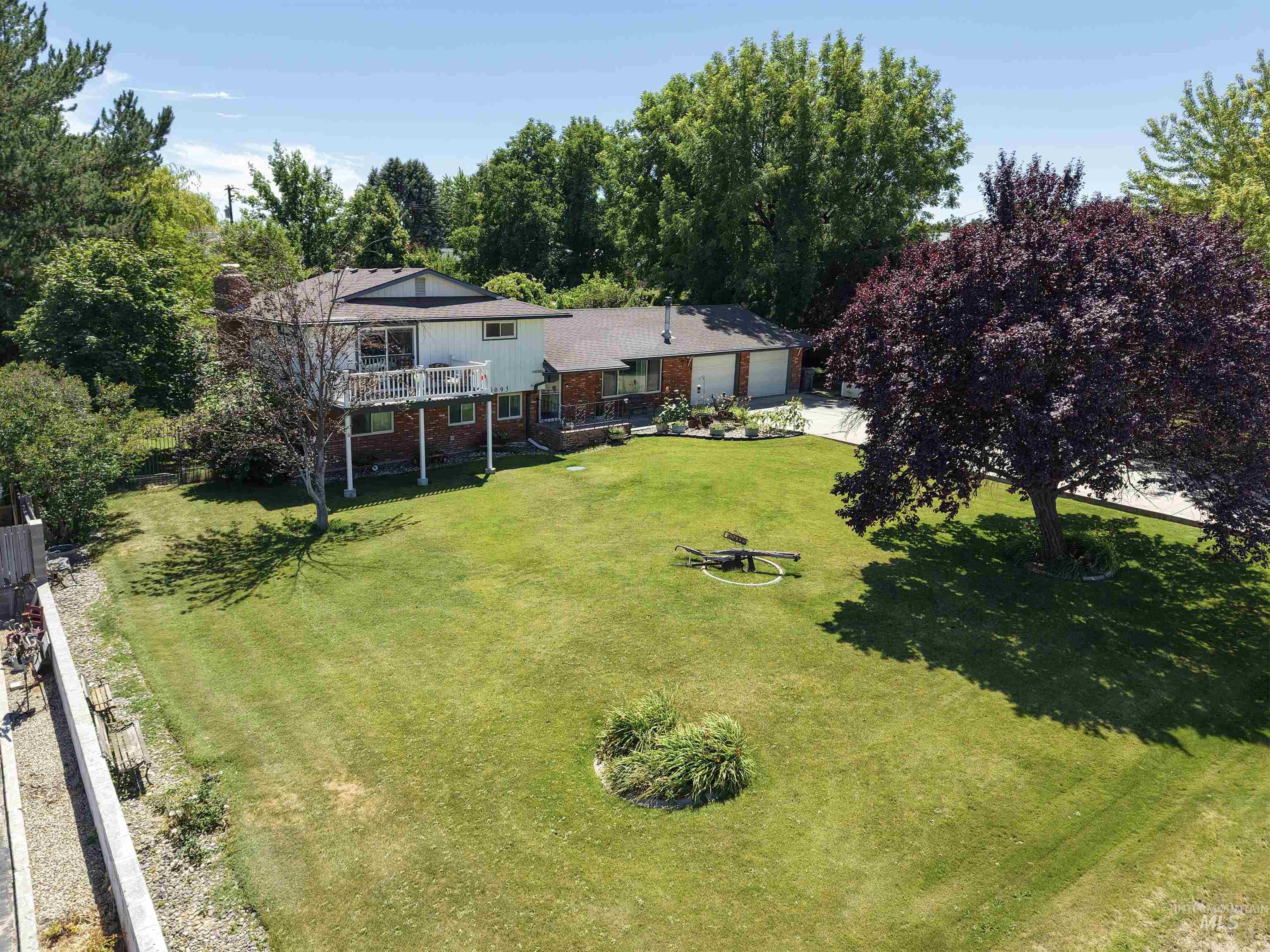15095 David Street Caldwell, ID 83607 - Photo 35 of 39 Expansive green lawn with mature trees and a two-story residence featuring a second-level balcony, lower-level patio, and an attached two-car garage