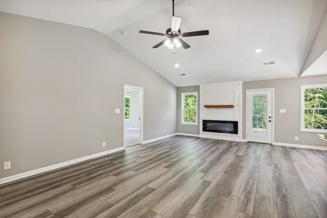 an empty room with wooden floor a ceiling fan and kitchen view